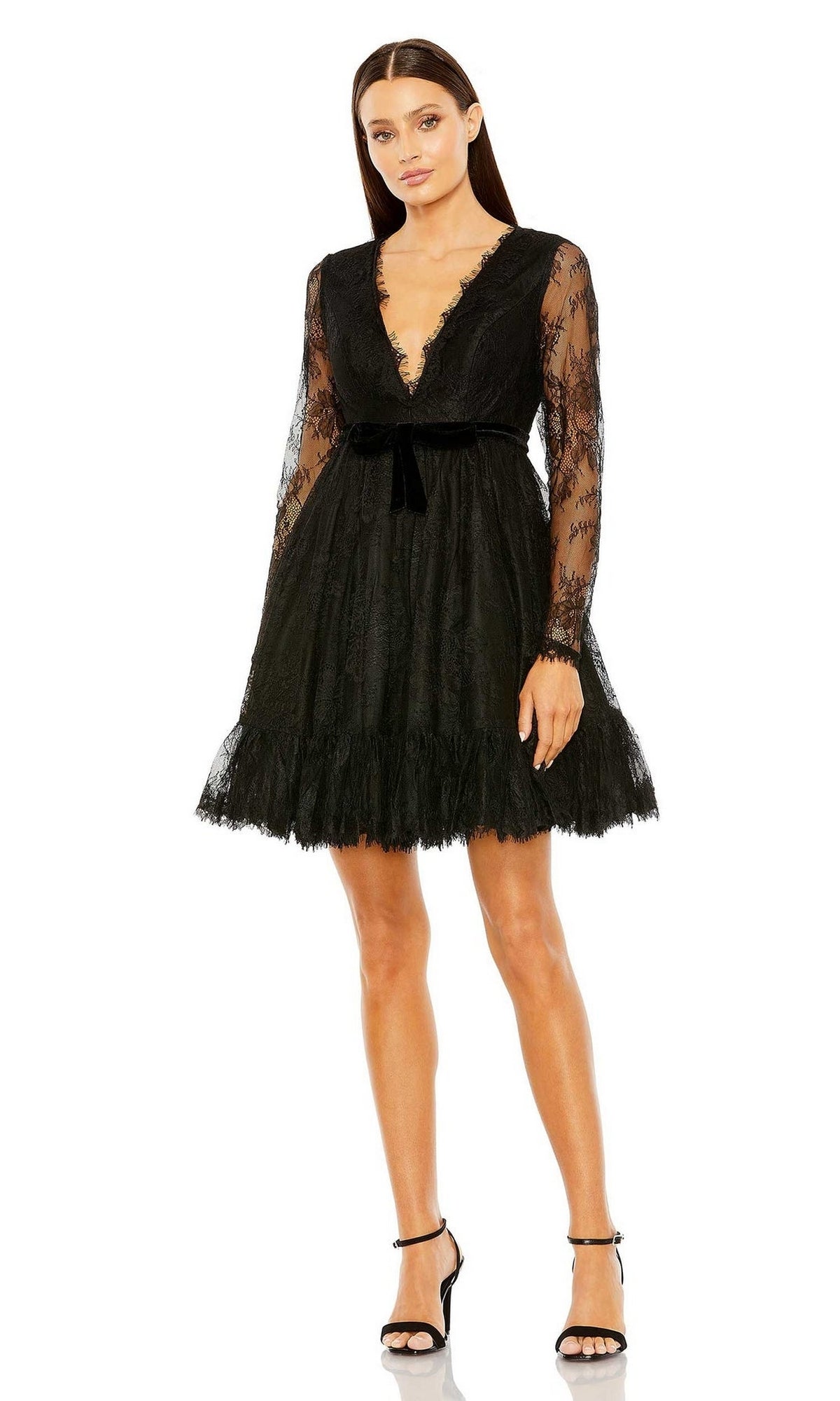 A woman in the Mac Duggal 49794 short black wedding guest dress stands against a white background, wearing black ankle-strap heels.